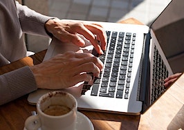 Hands typing on a laptop keyboard next to a cup of coffee