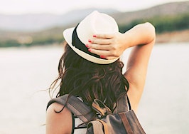 A millennial woman with her hand on a hat looking over a lake