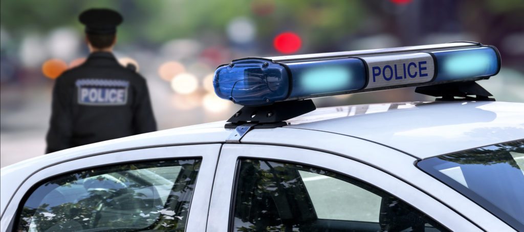 A police car with a policeman standing in front of it.
