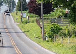 A horse and buggy driving down one side of a road with cars on the other side