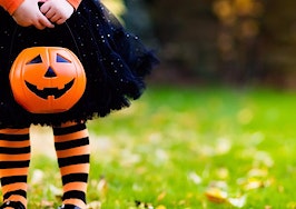 A young girl in a witch outfit with a Halloween candy pail